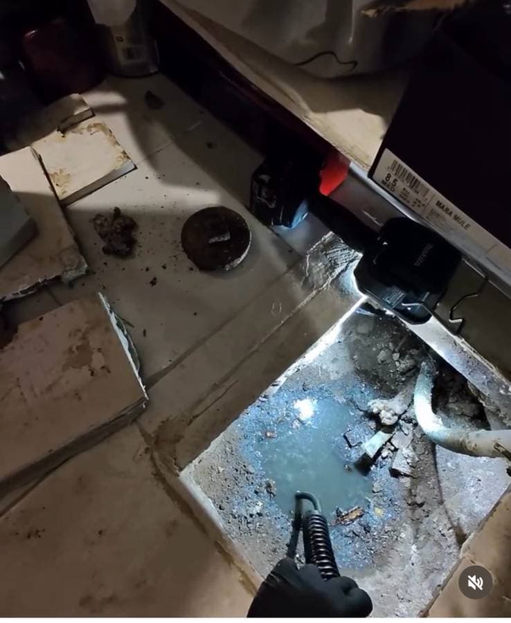 Open bathroom floor with exposed drain pipe and water visible during plumbing repair work