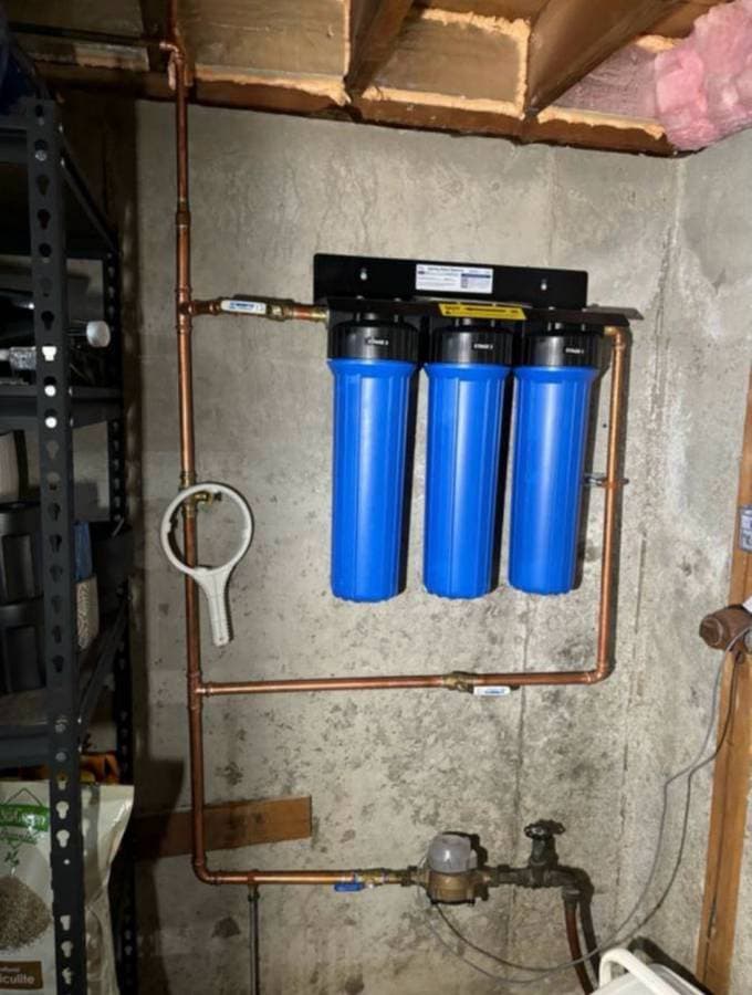 Whole-house water filtration system with blue filter canisters installed in basement