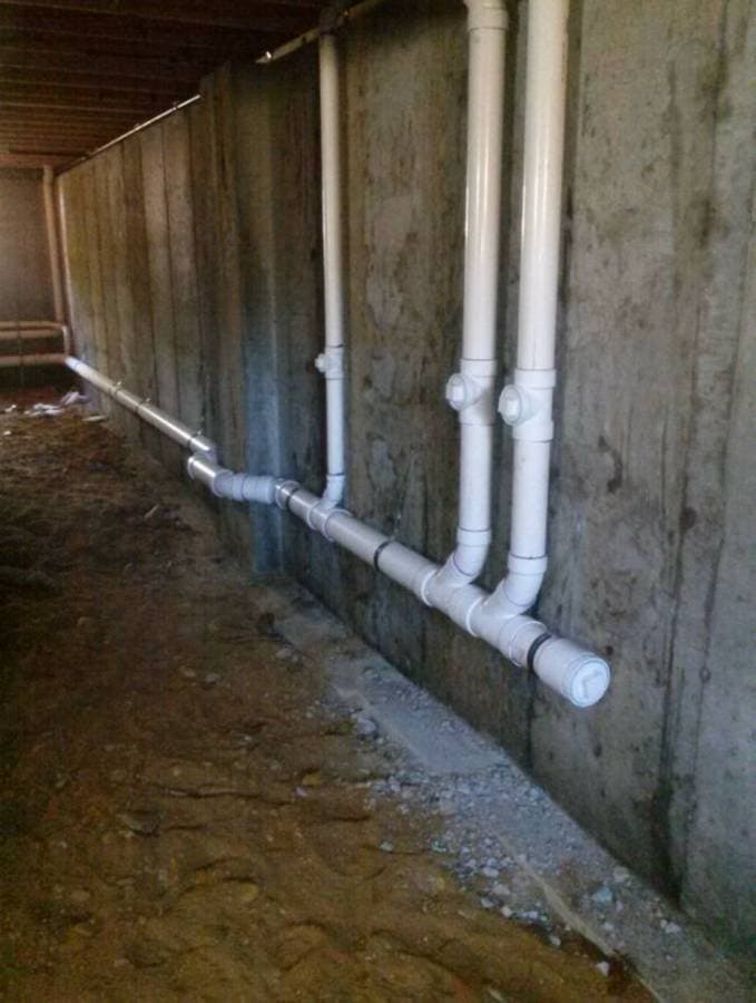 Newly installed PVC drain pipes running along basement wall after plumbing upgrade