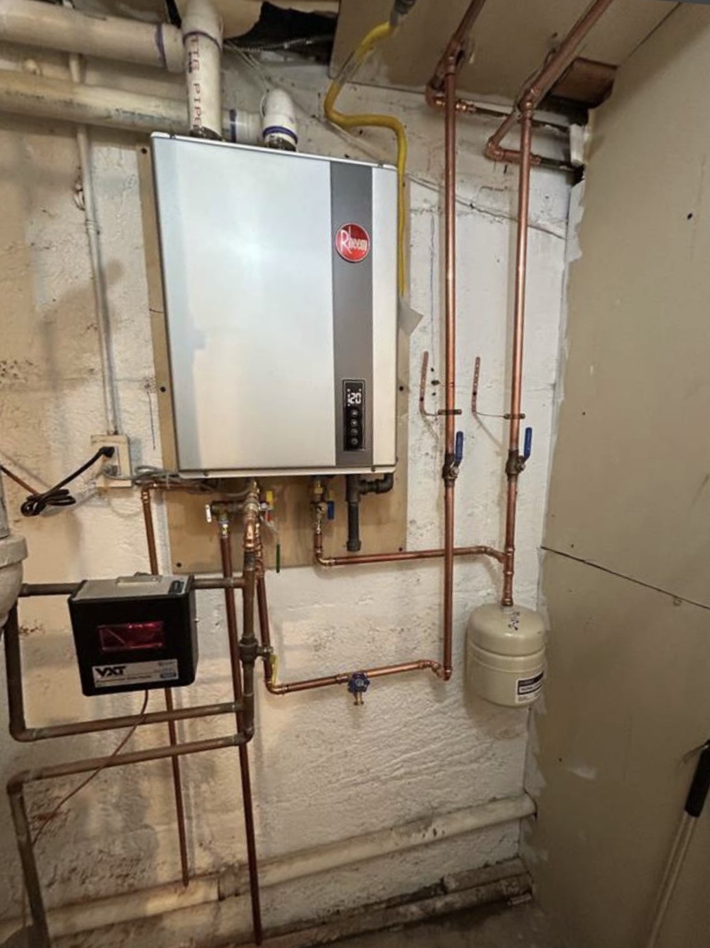 Tankless water heater installation with copper piping and expansion tank in residential basement utility room