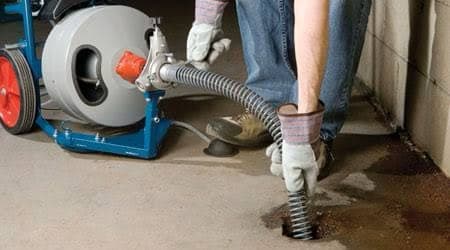 Plumber using a drain cleaning machine to clear a clogged pipe inside a residential home